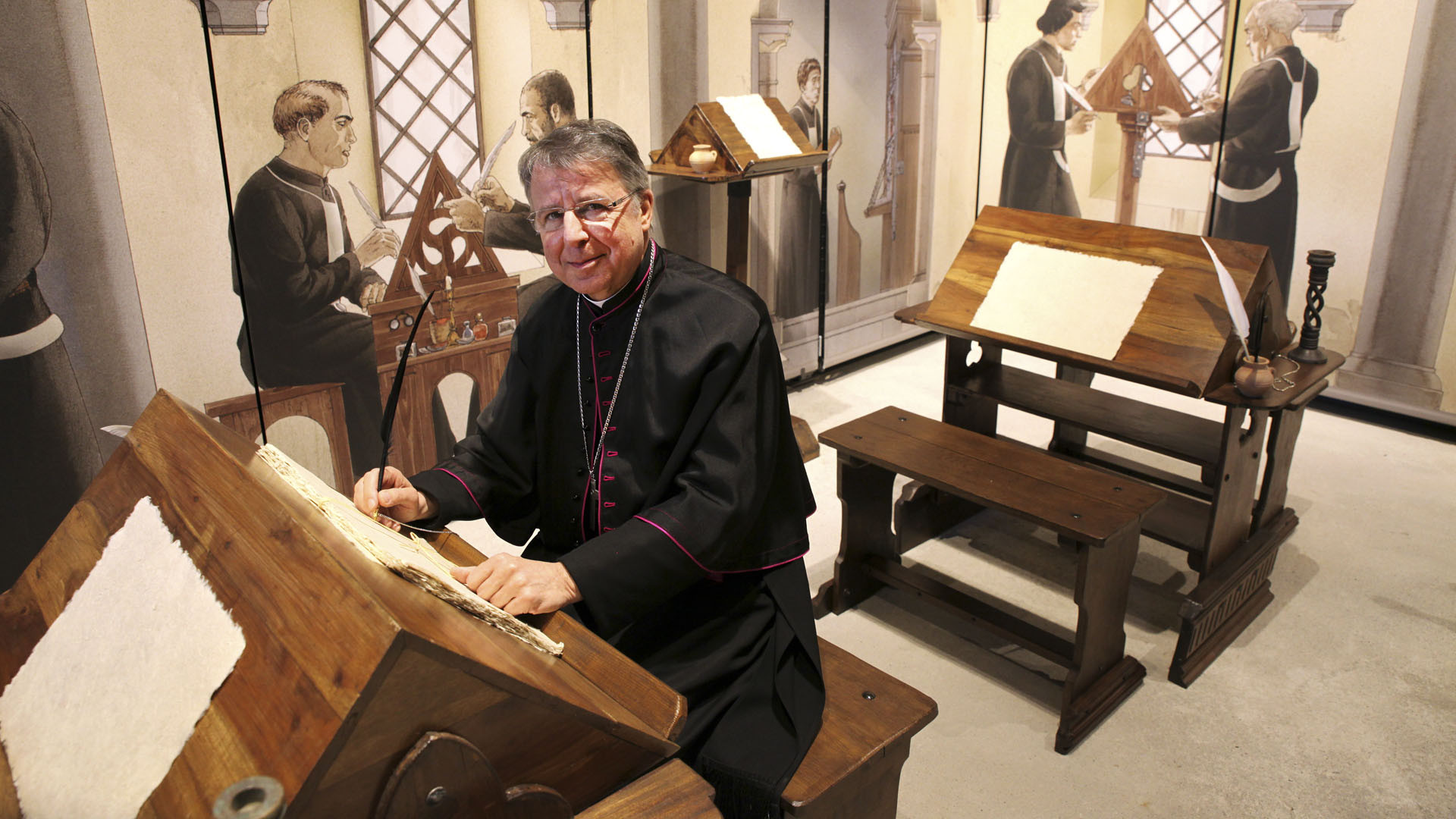 Saint-Maurice le 22 mars 2016. Exposition "Ecrire au Moyen-Age" dans le Clocher de l'abbaye. 2e étage du clocher, au scriptorium reconstitué. Mgr Jean Scarcella a repris la plume le temps d'une photo souvenir. (Photo: Bernard Hallet)